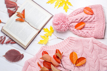 Book and a warm knitted hat and sweater, on an autumn wooden white table