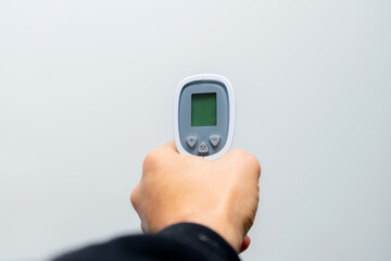 Doctor hand holding temperature gun on grey background. Close up of hand pointing thermometer in a hospital.