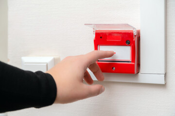 Hand pressing fire alarm button at school or business office. Close up of protection console...
