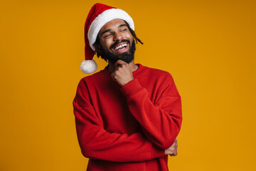 Joyful african american guy in Santa Claus hat smiling and looking aside