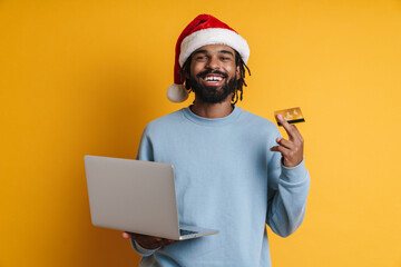 Joyful african american guy posing with laptop and credit card