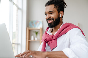 Happy african american guy in earphones working with laptop