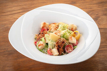 Classic Caesar Salad with grilled chicken, croutons, cherry tomatoes in a white plate on a wooden table