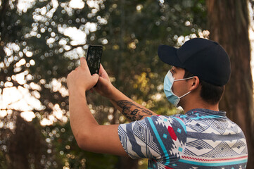 Man wearing a face mask taking a picture with his cellphone in the forest 