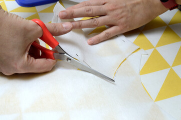 Women's hands cut the fabric with scissors according to the pattern on the table.