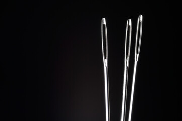 three sewing needles without thread on a dark background. macro.