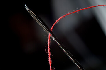 Needle and red thread on black background