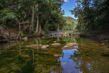 Obraz premium A beautiful mountain stream in the Cuban tropics. Clear water flows from the mountains forming small puddles and lakes. Perfect reflection.