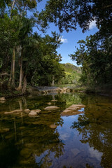 Fototapeta na wymiar A beautiful mountain stream in the Cuban tropics. Clear water flows from the mountains forming small puddles and lakes. Perfect reflection.