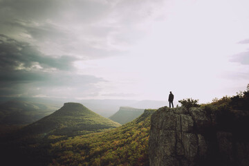 Man standing on the edge of a cliff with an atmospheric mountain landscape backdrop. Place your text here