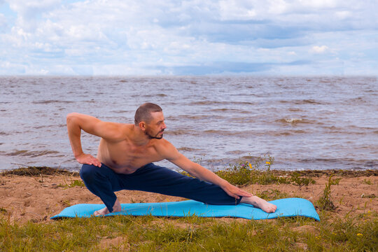 A European Man, 40 Years Old, Is Doing Yoga On The Seashore.