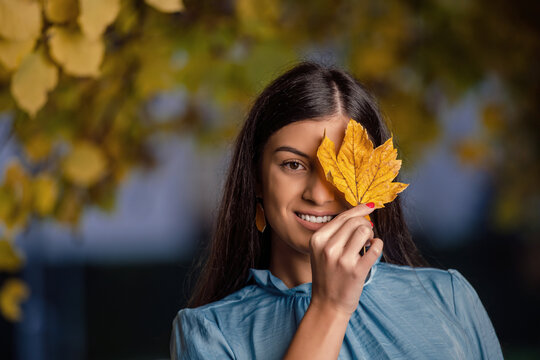 Beautiful young woman laying and smiling on the oak and maple leaves in the park.