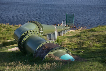 Close up image of huge industrial green metal pipe, running into water