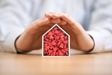 Wooden house with many red hearts protected by hands