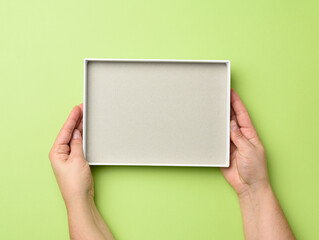 two female hands hold an open blank paper box on a green background