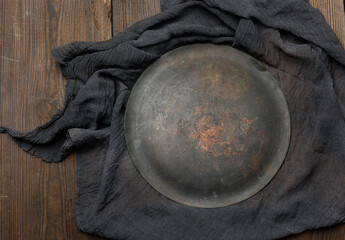 round plate  and black kitchen textile towel folded on a brown wooden table