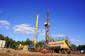 In a row are oil-producing wells. In the background, work is underway to overhaul the well. Drilling rig for drilling oil and gas wells with various equipment and materials.