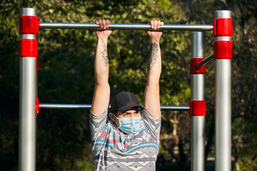 Man using his face mask doing pull ups in the park/gym
