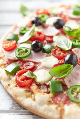Pizza with ham, mozzarella cheese, cherry tomatoes, green and jalapeno pepper, black olives and fresh basil. Bright background. Close up.	