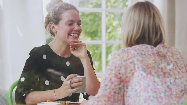 Two Female Friends In Coffee Shop Meeting Up In Socially Distanced Way Viewed Through Window - Shot In Slow Motion