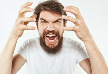 Emotional man gesticulates with his hands on a light background and a thick beard irritability