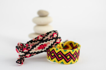 Two handmade homemade colorful natural woven bracelets of friendship with white river stone cairn tower isolated