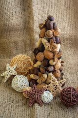 Christmas tree made of autumn ripened brown fruits on jute beige background, chestnuts cones beech nuts almonds walnuts peanuts