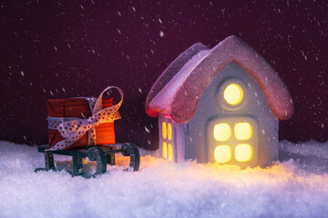 House in snow with glowing windows and gift box. Xmas and New Year Concept