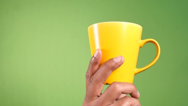 hand holding yellow coffee mug again green background 