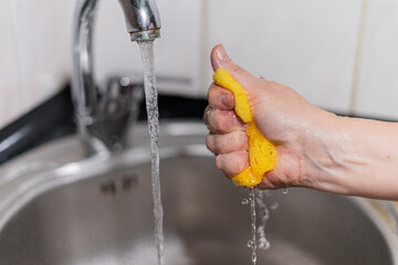 Yellow sponge for dishes under water in girl hand