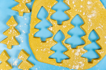 Gingerbread cookies in the form of fir trees on raw dough on a blue background.