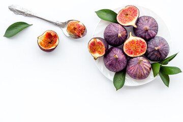 Fresh whole and sliced figs on a plate with green leaves. Top view