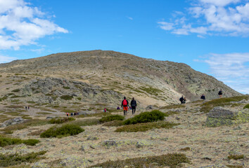 Fototapeta premium Hikers and hikers climbing the mountain on a trail on a sunny day. Ascent to Peñalara in the Sierra de Madrid.