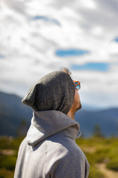 Young White Man From Behind With Sunglasses In Beautiful Natural Setting Surrounded By Mountains Looking Up At Cloudy Sky