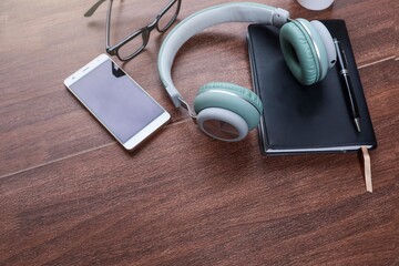 Headphones, notebook, smartphone, and eyeglasses on wooden table