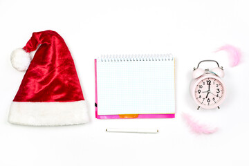 Santa cap, empty notepad and alarm clock on white. New year resolutions. Notepad with Christmas decorations. New year with new plans