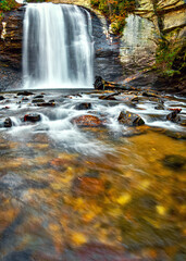 A vertical landscape of Looking Glass Falls waterfall in North Carolina with blurred rocky water in the foreground. Copy space.