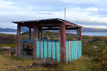 Dilapidated fishing hut on the ocean. Northern landscape with mountains, ocean and house.
