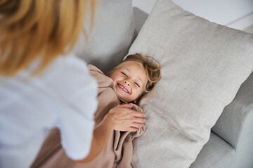 Happy smiling little girl lying on sofa while feeling good near her mother