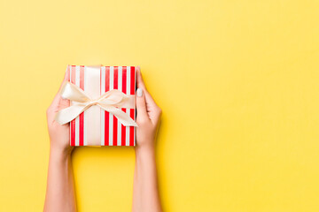 Woman arms holding gift box with colored ribbon on yellow table background, top view and copy space for you design