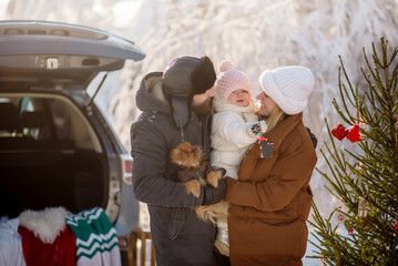 Young parents of the family are holding a little daughter and a dog on the background of Christmas...