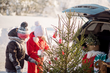 Brother and sister pick a Christmas tree and load it into the trunk of an SUV
