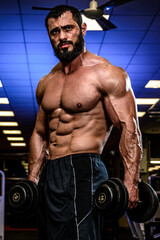 Fototapeta na wymiar handsome young bearded man with dumbbells in blue lit sport gym during heavy workout training