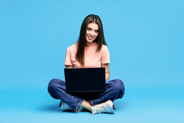 Portrait of happy young woman sitting on floor with legs crossed working on laptop