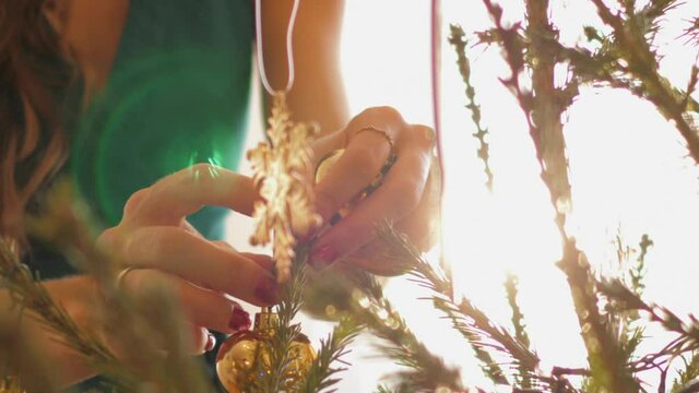 Woman with red nails and gold ring hangs Christmas toys in heart shape and snowflake at lens flare. Concept holiday