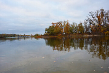 The beautiful bank of the Dnipro river with yellow, green, red trees, bushes with a pleasant autumn nature of the city of Kamianske, Ukraine.