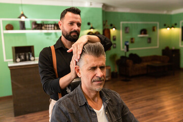 barber combs a man with gray hair and a goatee in a barber shop