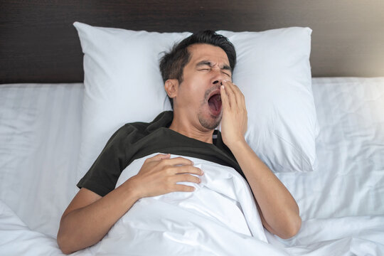 Asian man lying yawning And sleepy in a white bed