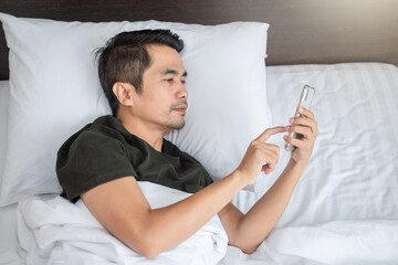 Asian man using smartphone at white bed