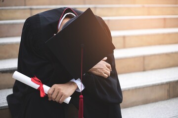 Men wearing university graduation gowns, anxiety, stress sitting on stair, concept of business...